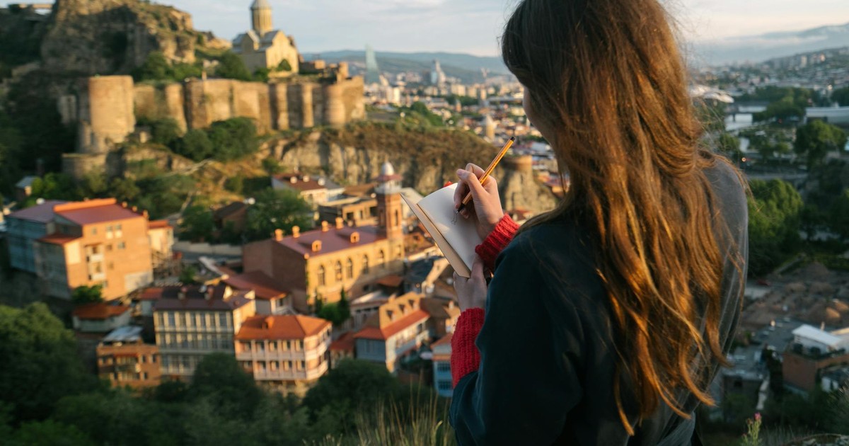 Woman writing in journal with a historic city view in the background, capturing inspiration from a stunning cityscape.