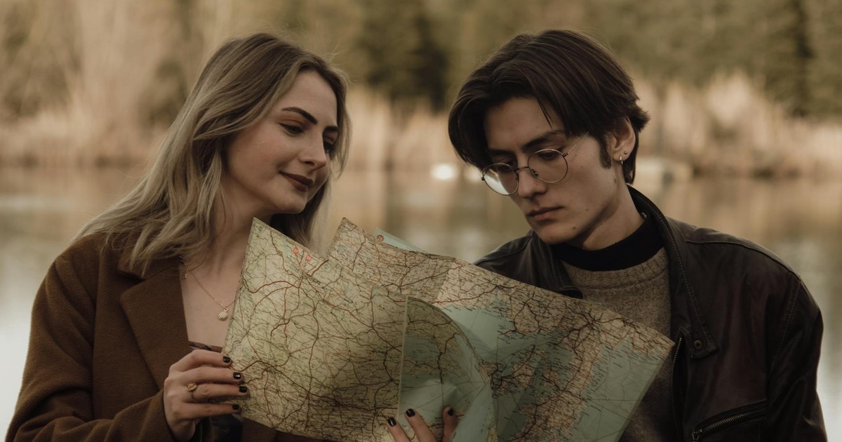 Young couple analyzing a map by a serene lake, planning their travel route in a tranquil nature setting.