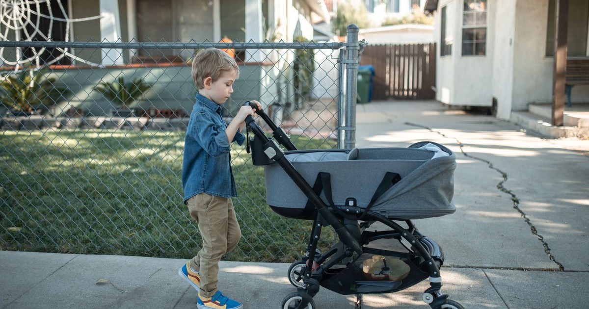 A young boy pushing a baby stroller along a suburban sidewalk on a sunny day.