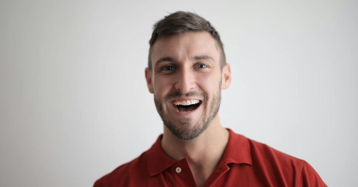 A cheerful man smiling broadly in a red polo shirt against a white background.