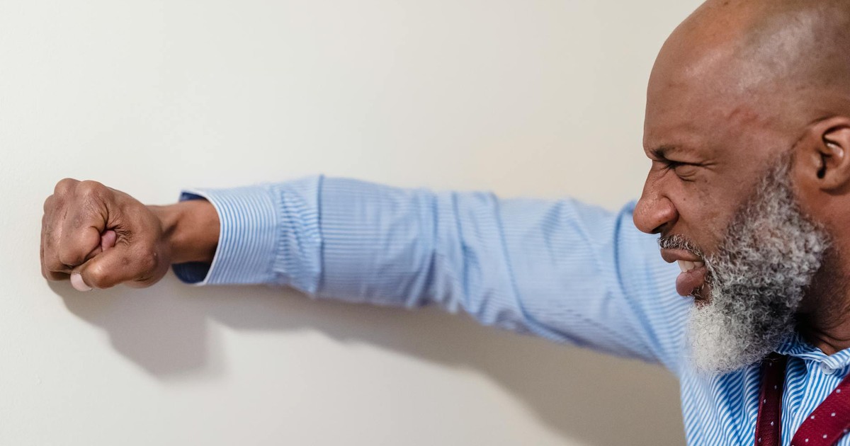 An adult man expressing frustration and anger by punching a wall indoors.