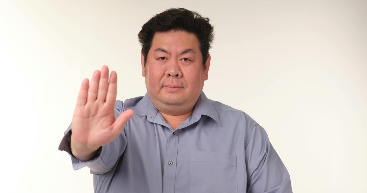 Portrait of a man in blue shirt gesturing stop with hand, studio background.