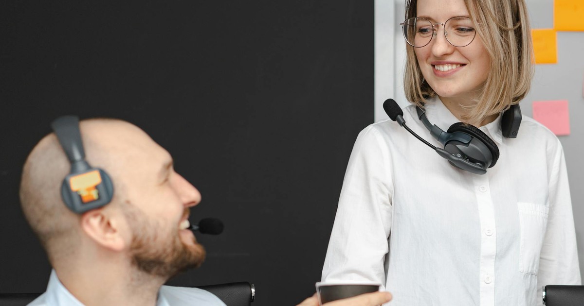 Two call center colleagues with headsets smiling and interacting in an office environment.