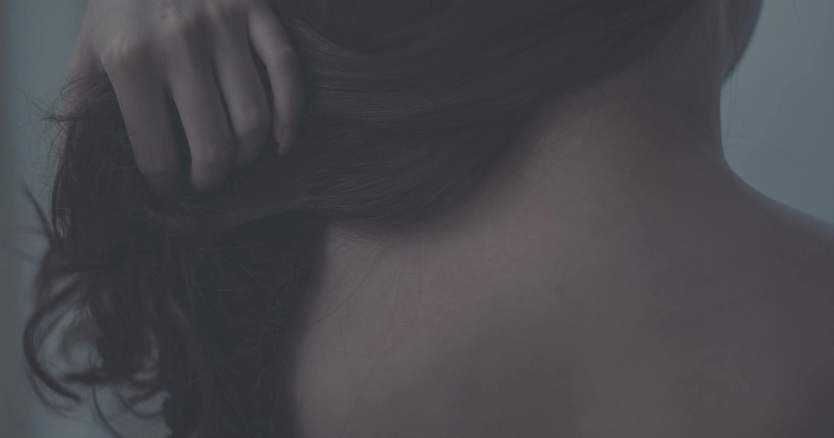 Artistic close-up of a woman gently touching her hair, capturing soft textures and intimate mood.