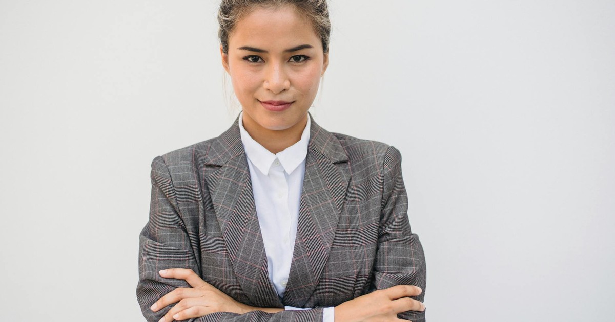Portrait of a confident Asian woman in a plaid blazer with arms crossed, smiling and posing.