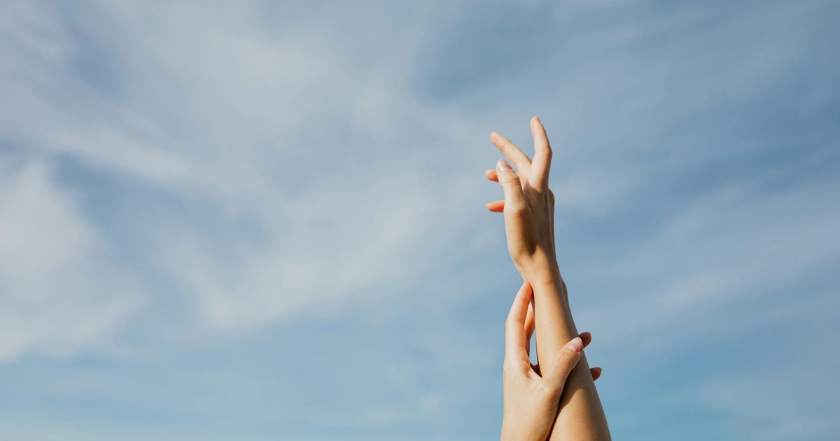 Two adult hands reaching up in front of a clear blue sky, symbolizing freedom and aspiration.