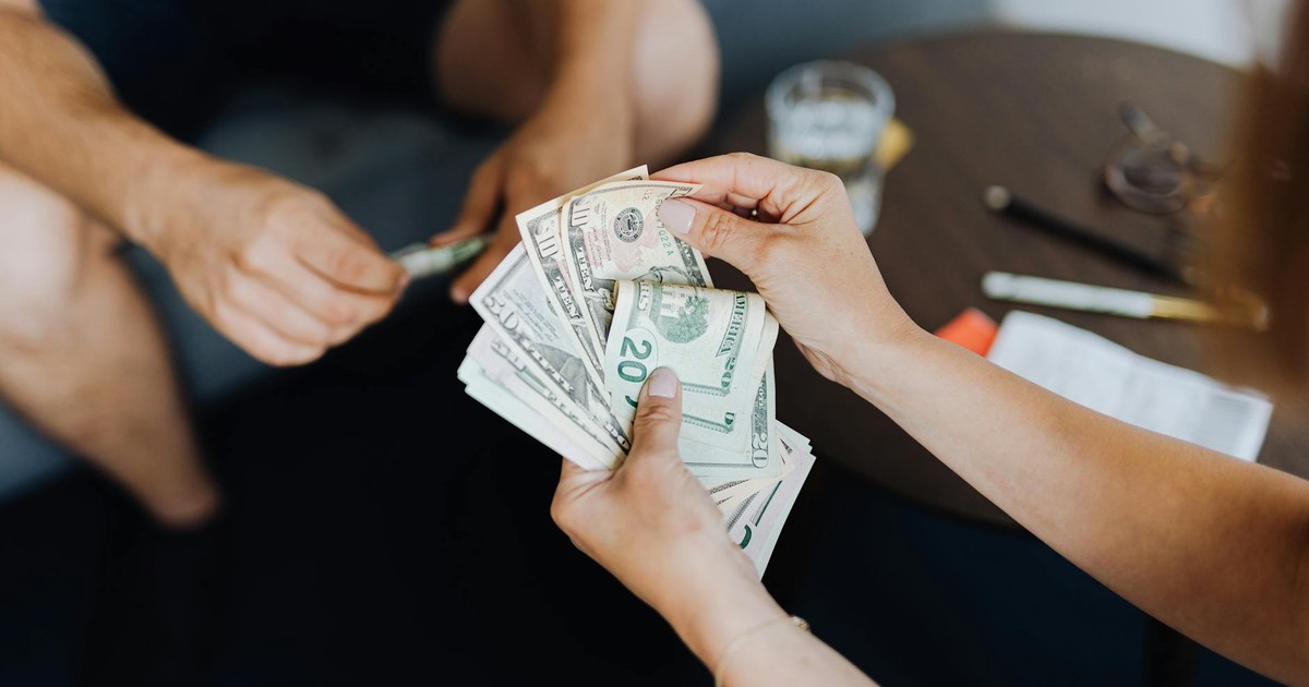 Close-up of people handling and counting US dollar bills indoors.
