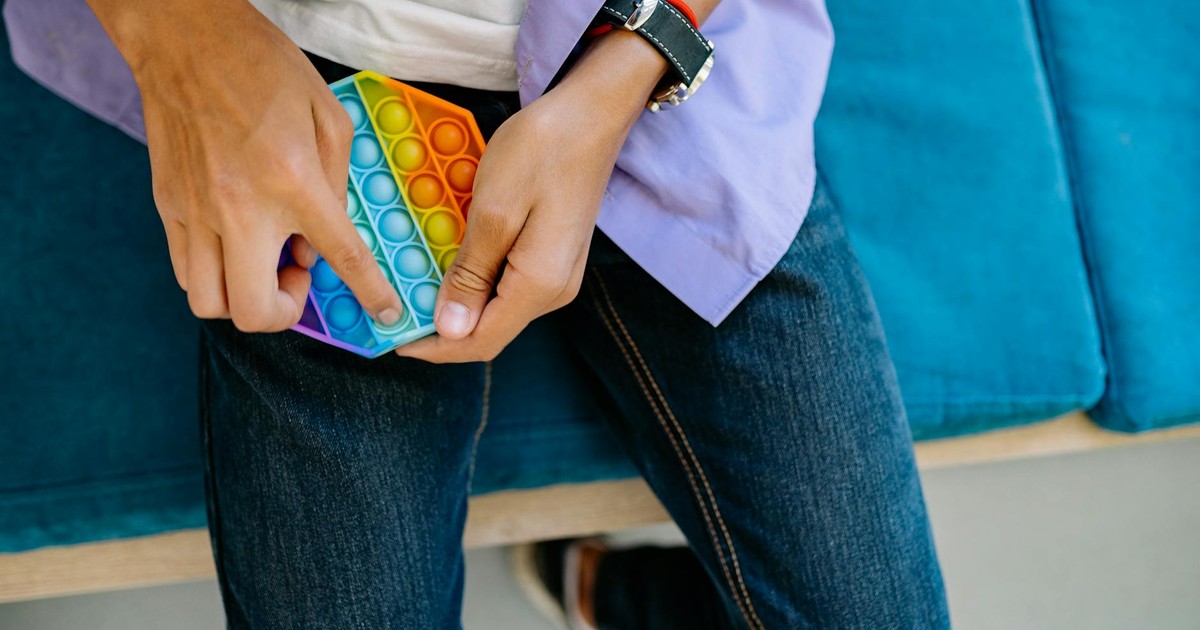Close-up of person playing with a colorful Pop It toy on denim jeans while sitting.