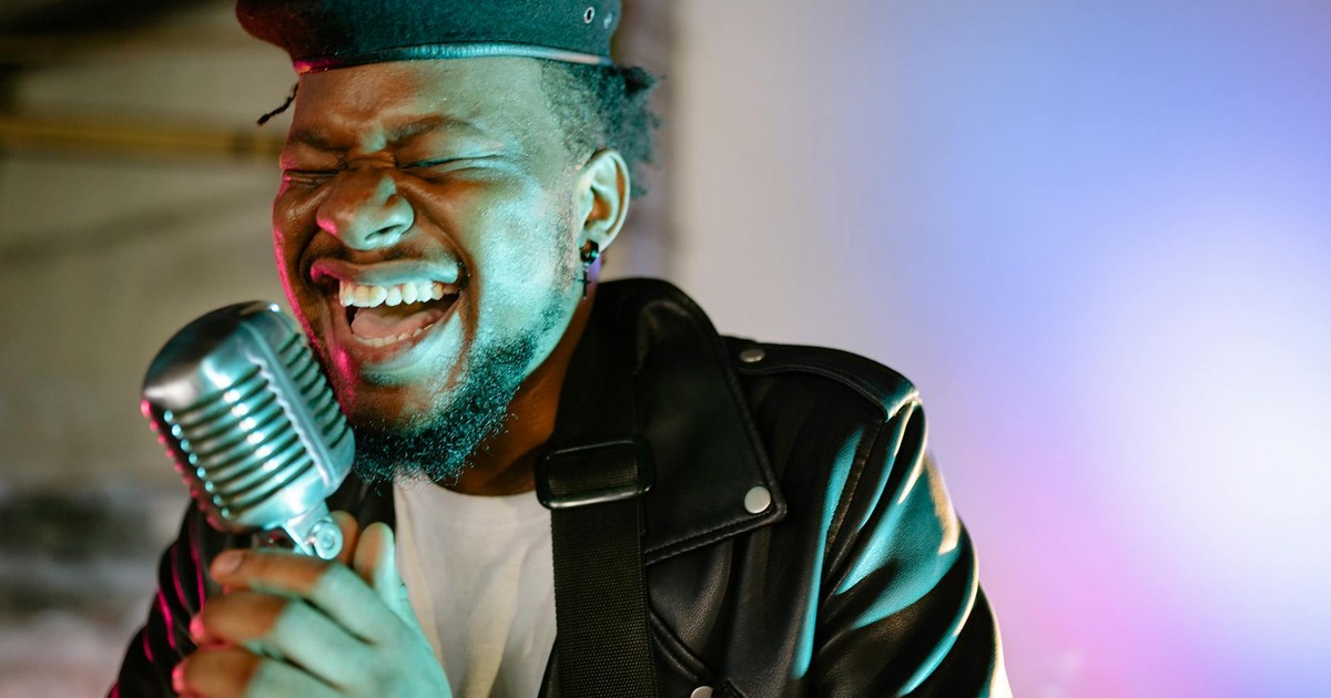 Dynamic portrait of an African American man passionately singing with a microphone under colorful stage lights.