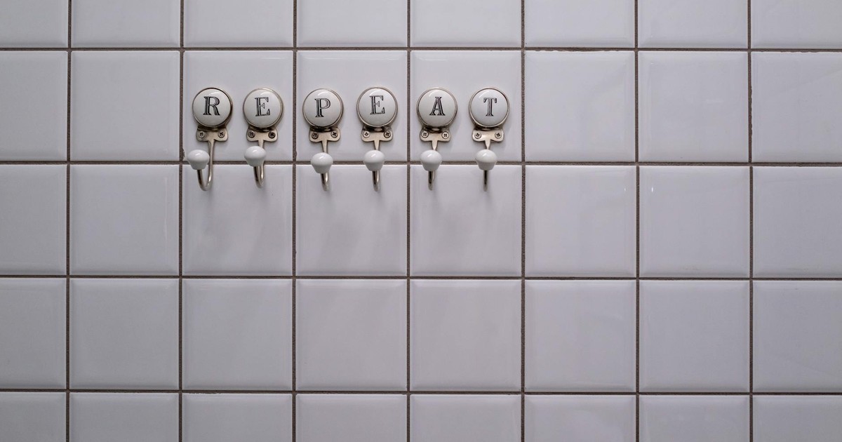 White tiled wall with towel hooks spelling 'REPEAT', showcasing a conceptual minimalist design.
