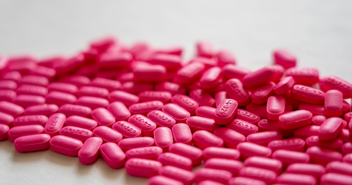 A detailed close-up of vibrant neon pink pills spread on a white table surface.
