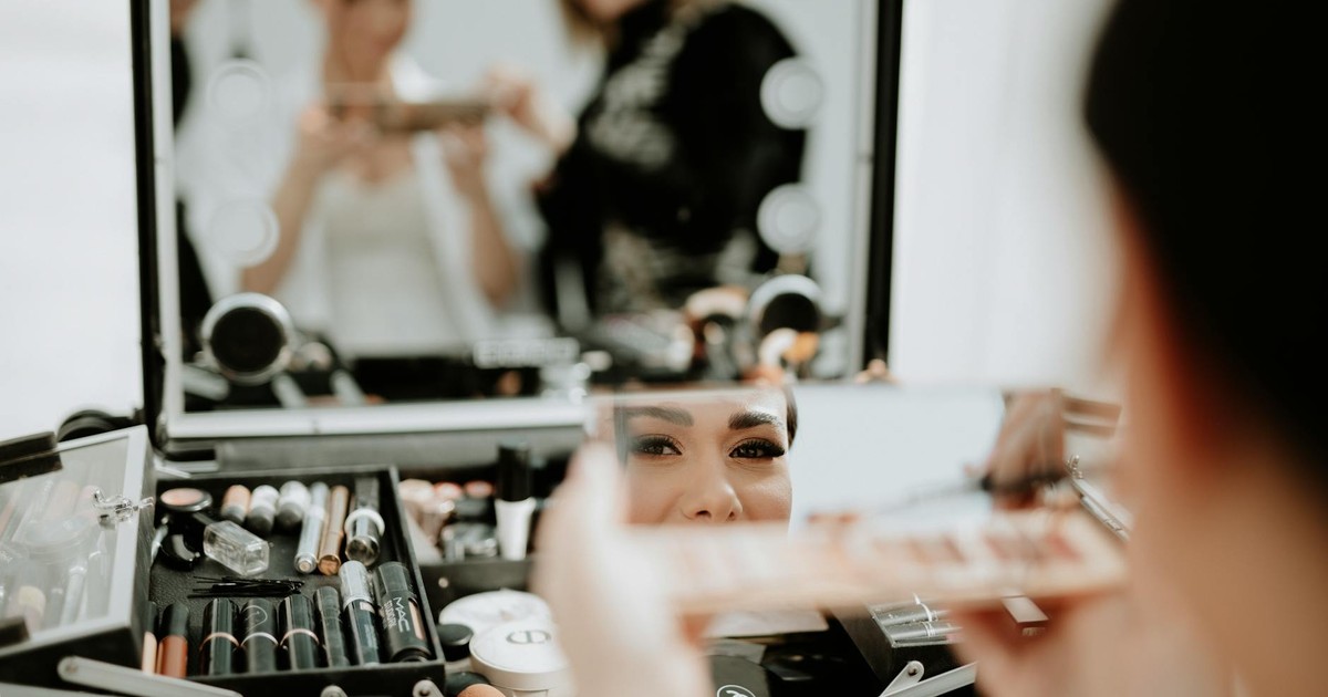 Bride getting her makeup done with a beautician in front of a mirror. Focus on reflection.