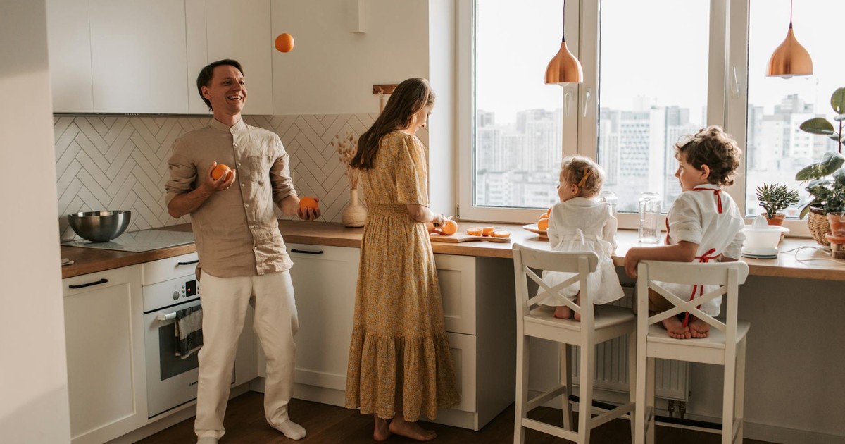 Family enjoying a playful morning in a sunlit modern kitchen with city view.