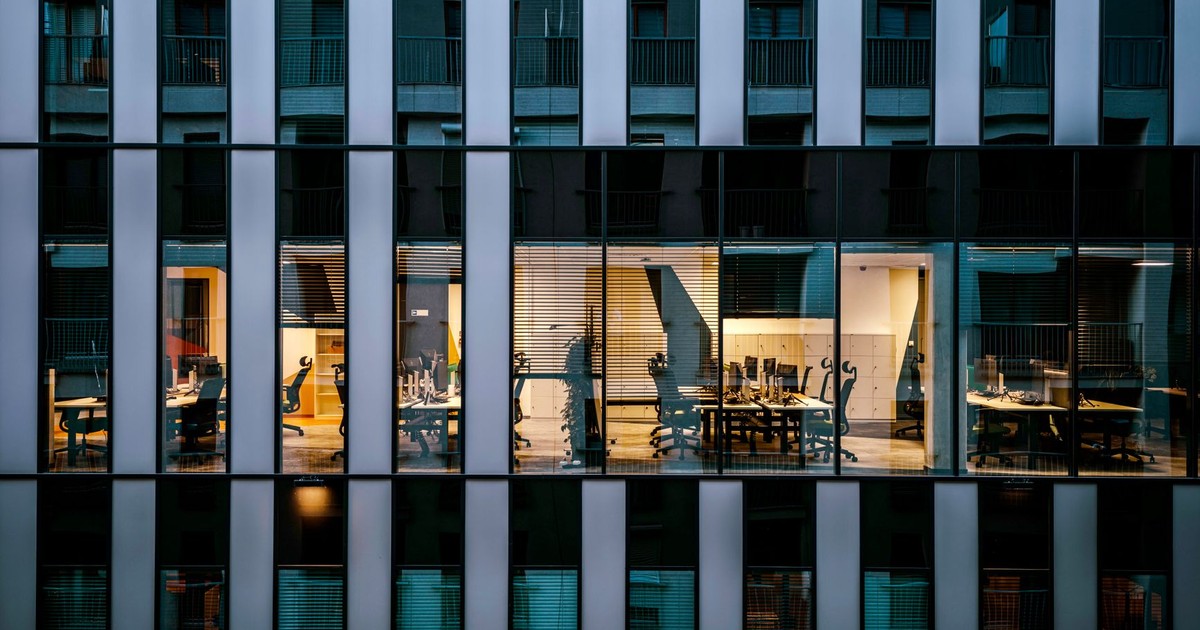 Illuminated office inside a modern glass building exterior, showcasing architecture and workspace design.