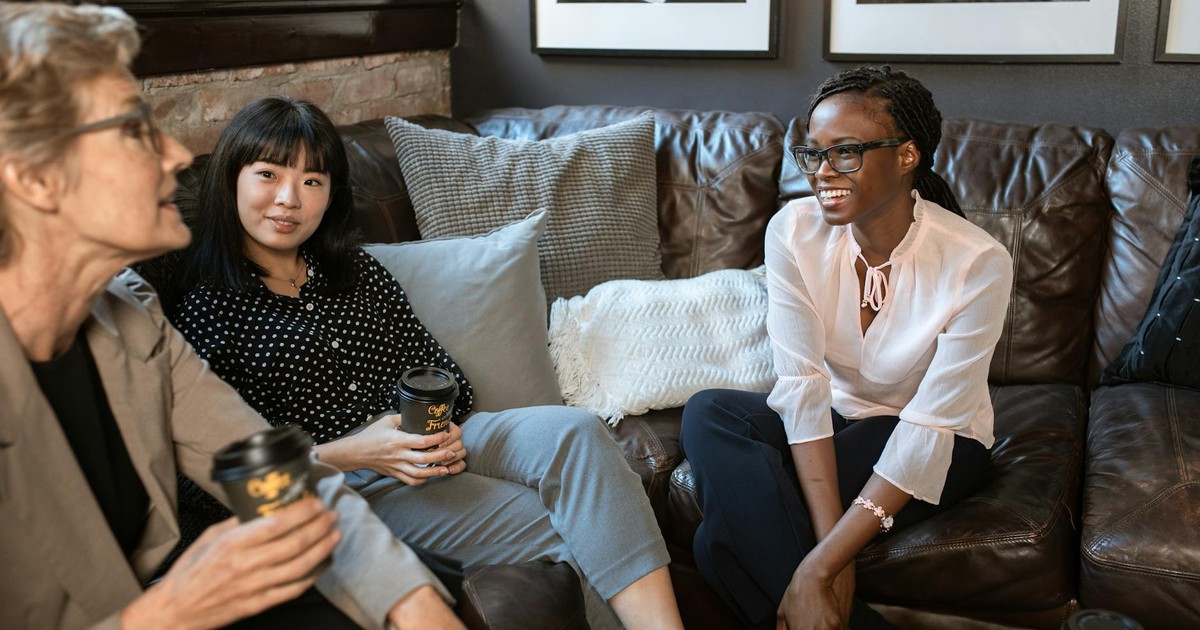 Three women in a cozy setting having a casual conversation with coffee.