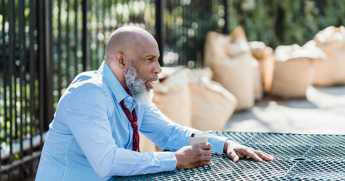 Side view of concerned African American male entrepreneur in formal clothes with can of alcohol beverage sitting at table on street