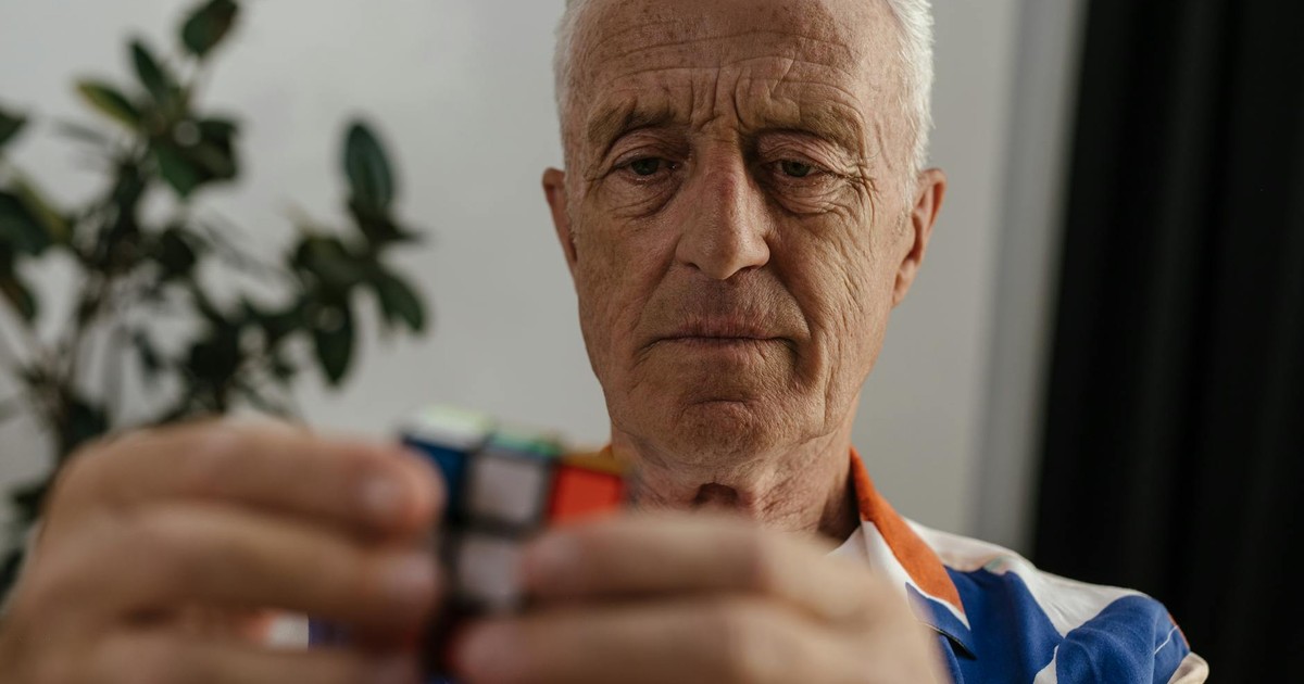 Elderly man concentrating on solving a Rubik's Cube, showcasing focus and mental agility.
