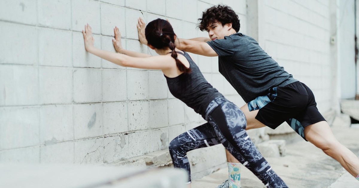 Man and woman stretching against a wall outdoors, showcasing athletic strength and teamwork.