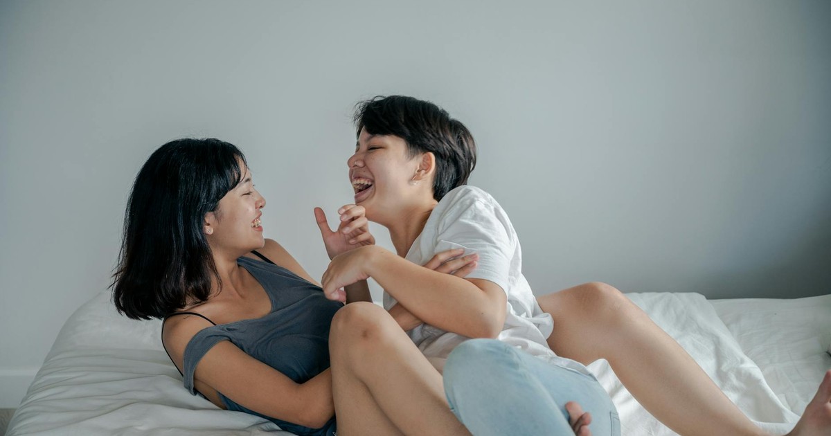 Two women sharing a joyful and intimate moment on a bed indoors.