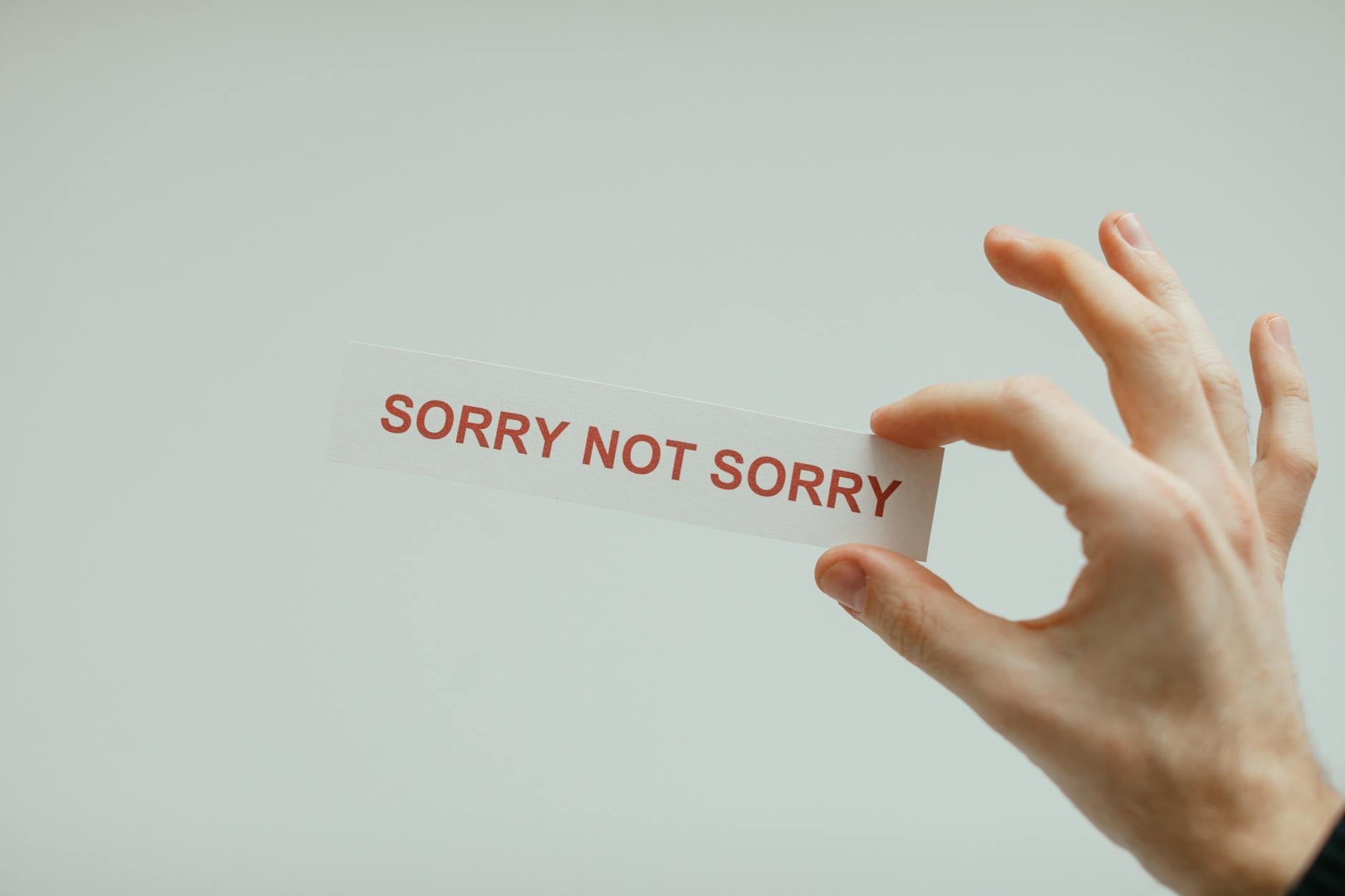 Hand holding a card with the phrase 'Sorry Not Sorry' on a neutral background.