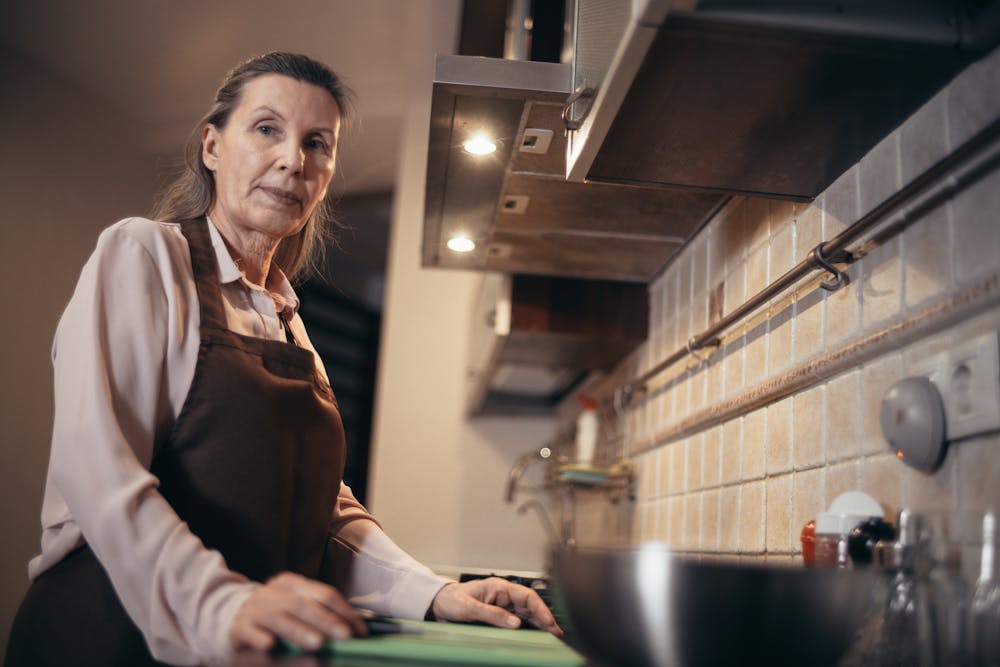 A mature woman in an apron stands confidently in a modern kitchen interior