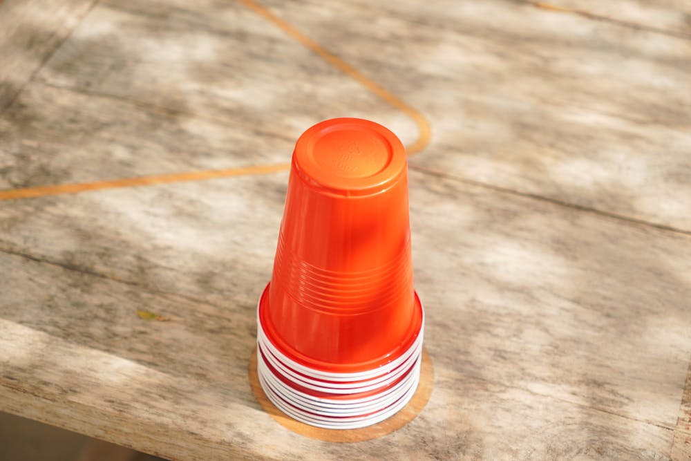 A stack of vibrant red plastic cups placed on a wooden table in outdoor sunlight