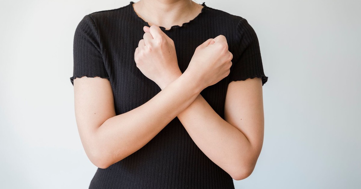 A woman in a black shirt crossing her arms in front of a plain white background.
