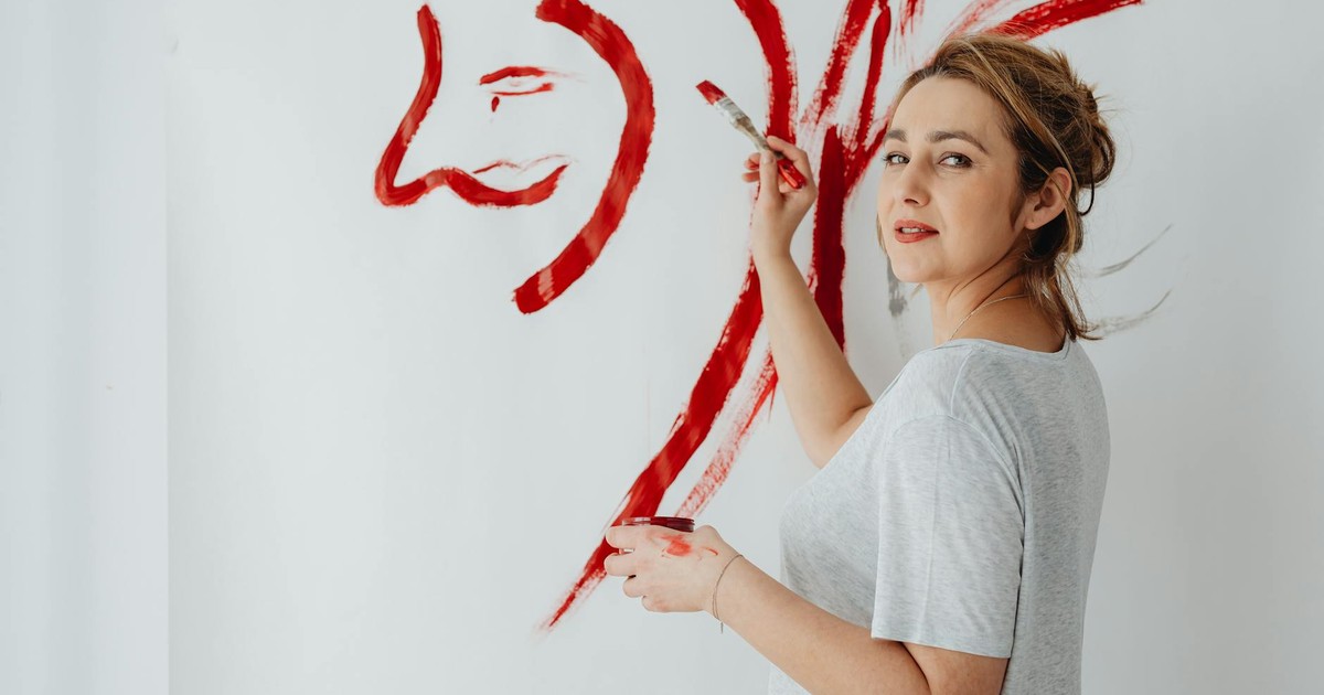 Female artist painting an abstract portrait on canvas with bold red strokes.