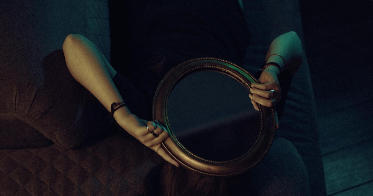 An enigmatic scene of a woman lying on a couch holding a mirror, creating a sense of intrigue.