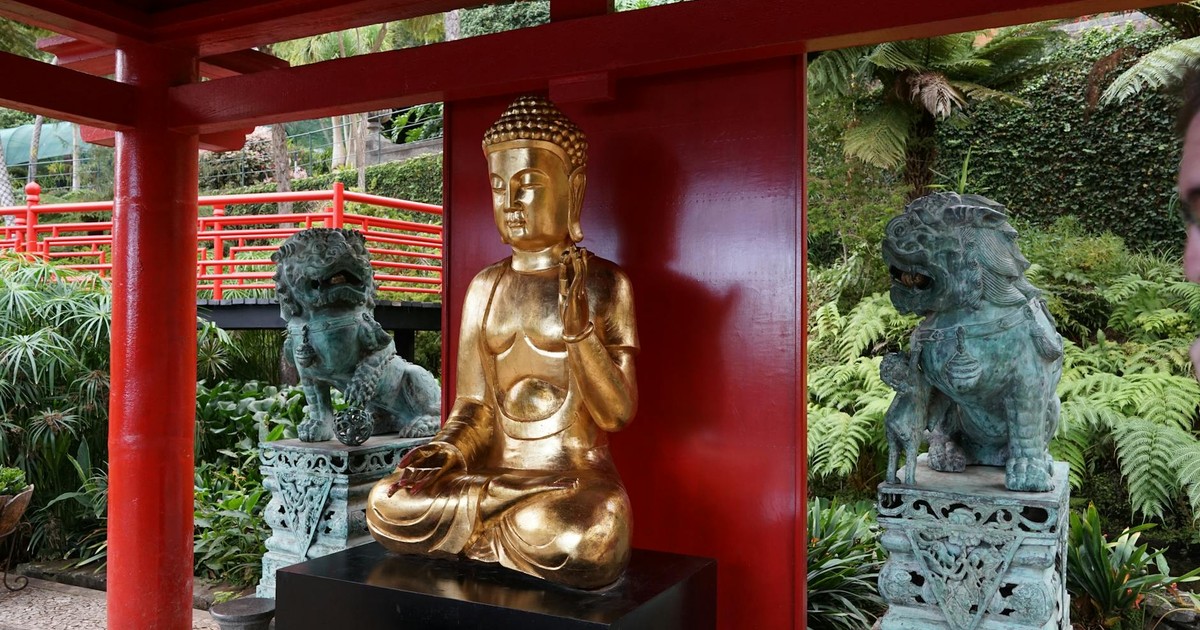Golden Buddha statue with surrounding lion statues in a serene garden with red wooden beams.