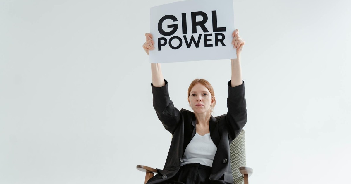 Confident woman in blazer sits with 'Girl Power' sign on white background.