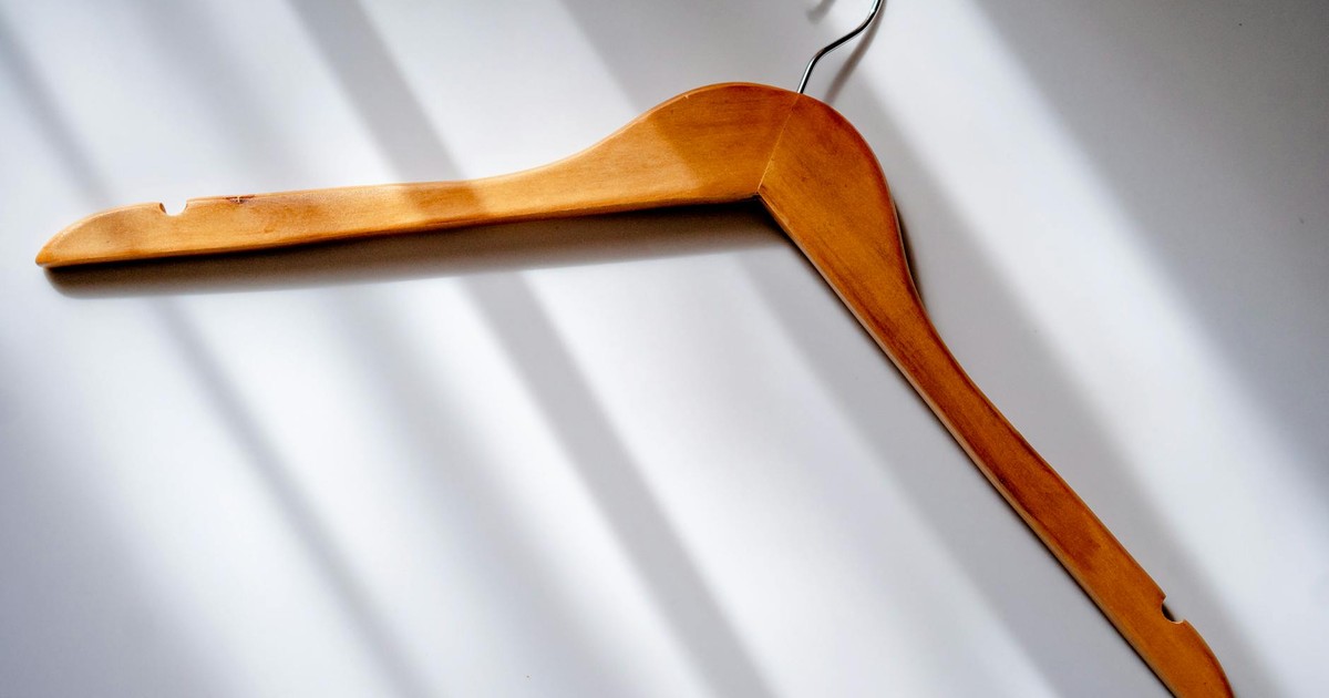 Minimalist image of a wooden clothes hanger casting shadows on a white surface.