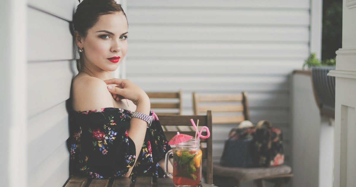 Elegant woman in floral dress enjoying a refreshing drink on a patio.