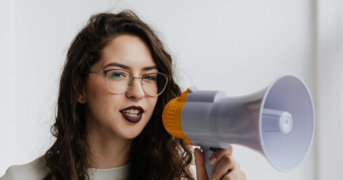 Confident woman with eyeglasses speaking into a megaphone in a bright room.