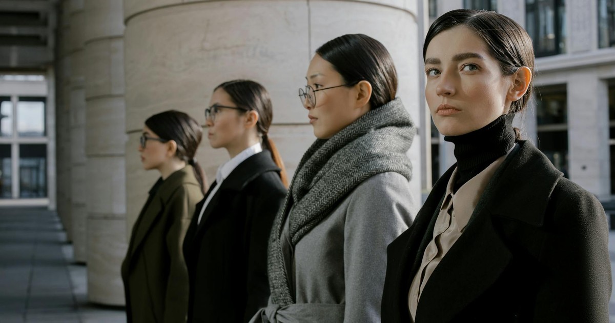 Four professional women in elegant coats walking in an urban setting, showcasing diversity and style.