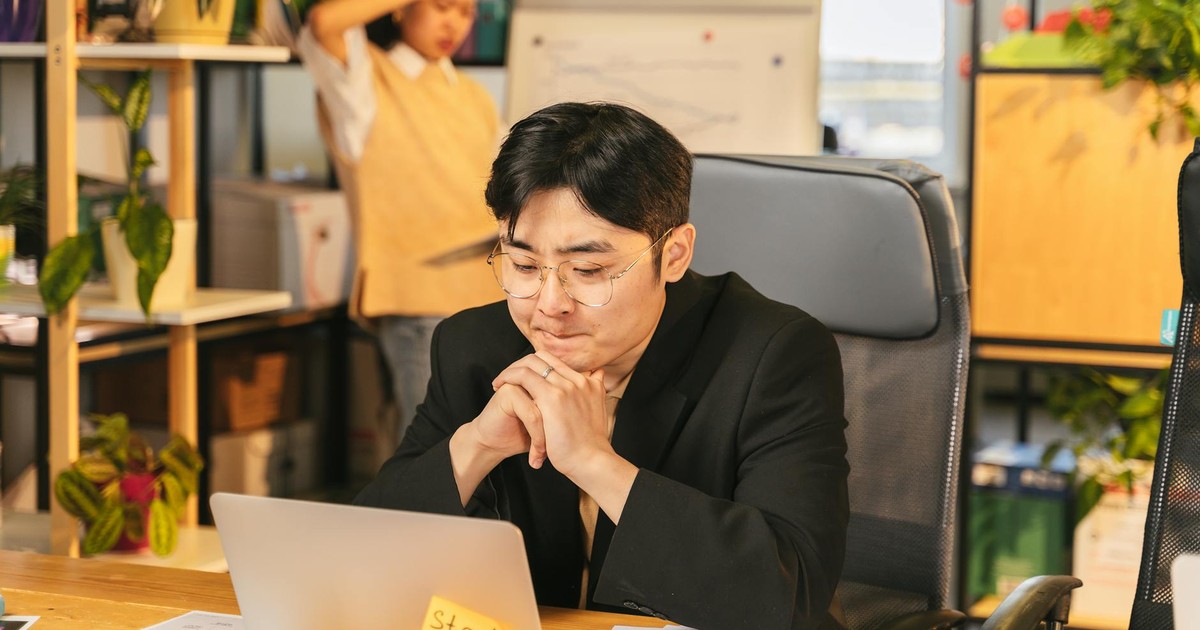Young professional deep in thought while working on a laptop in a modern office workspace.