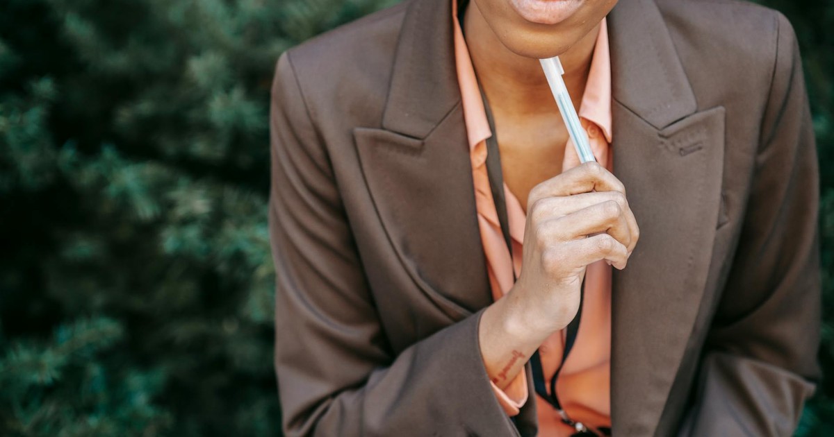 High angle of crop female entrepreneur in formal wear touching chin with pen while thinking on solution in park