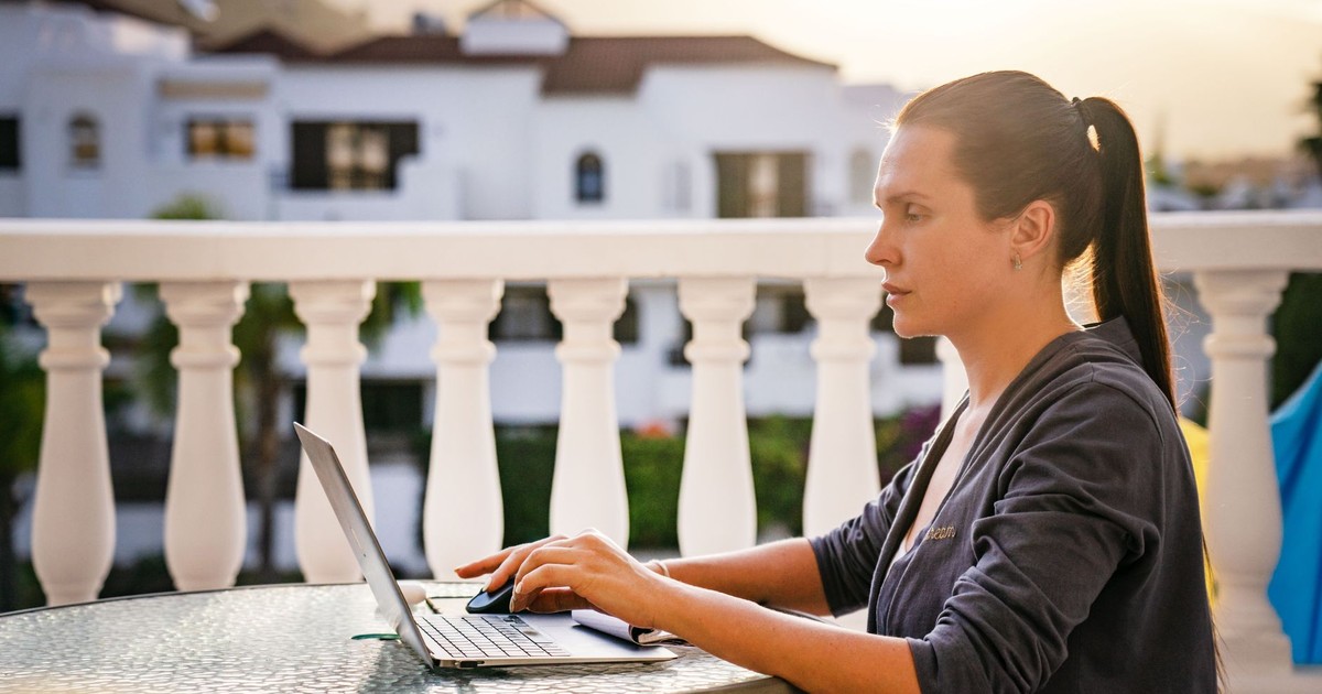 A focused woman works on her laptop outdoors on a sunny balcony, capturing a serene morning work vibe.