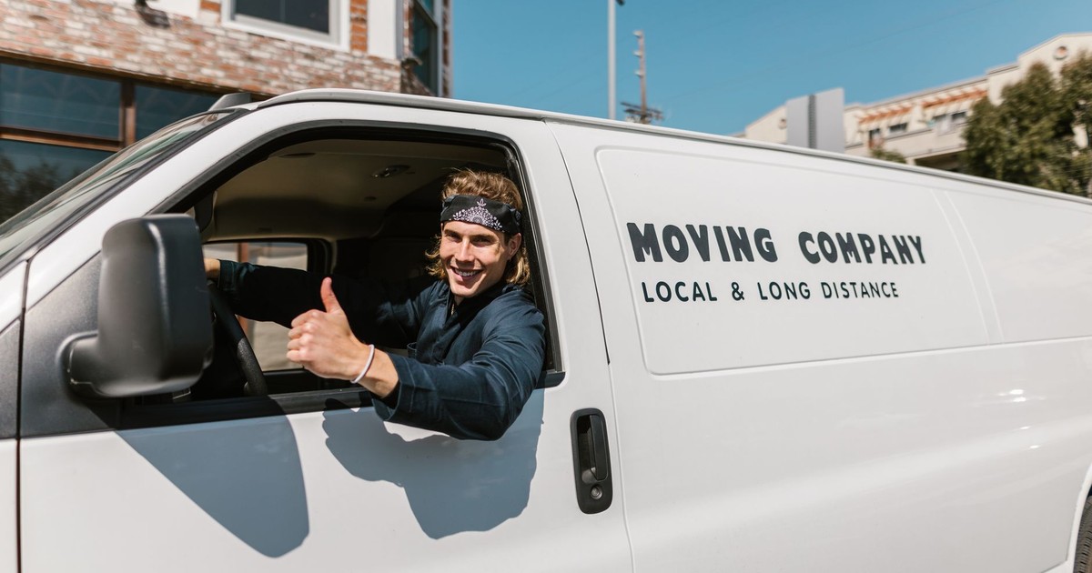 Smiling mover giving thumbs up from a moving company van parked outside.
