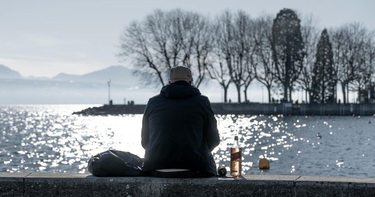 A solitary man in a jacket facing a body of water in a park, reflecting on life.