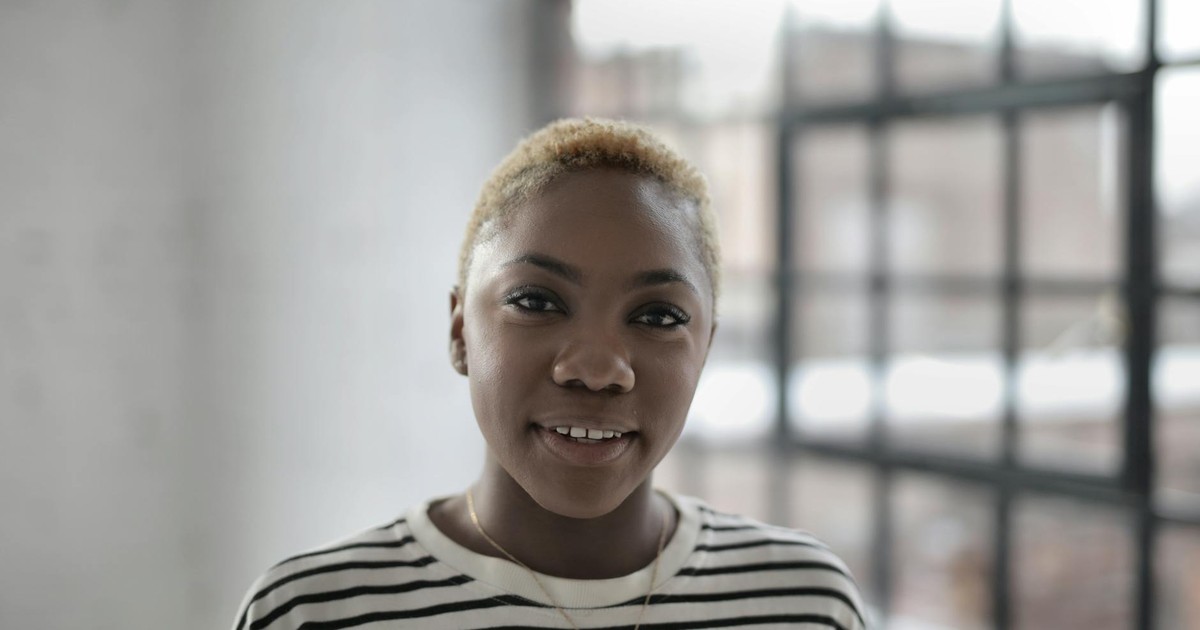 Portrait of a smiling woman with short hair in a bright room with large windows.