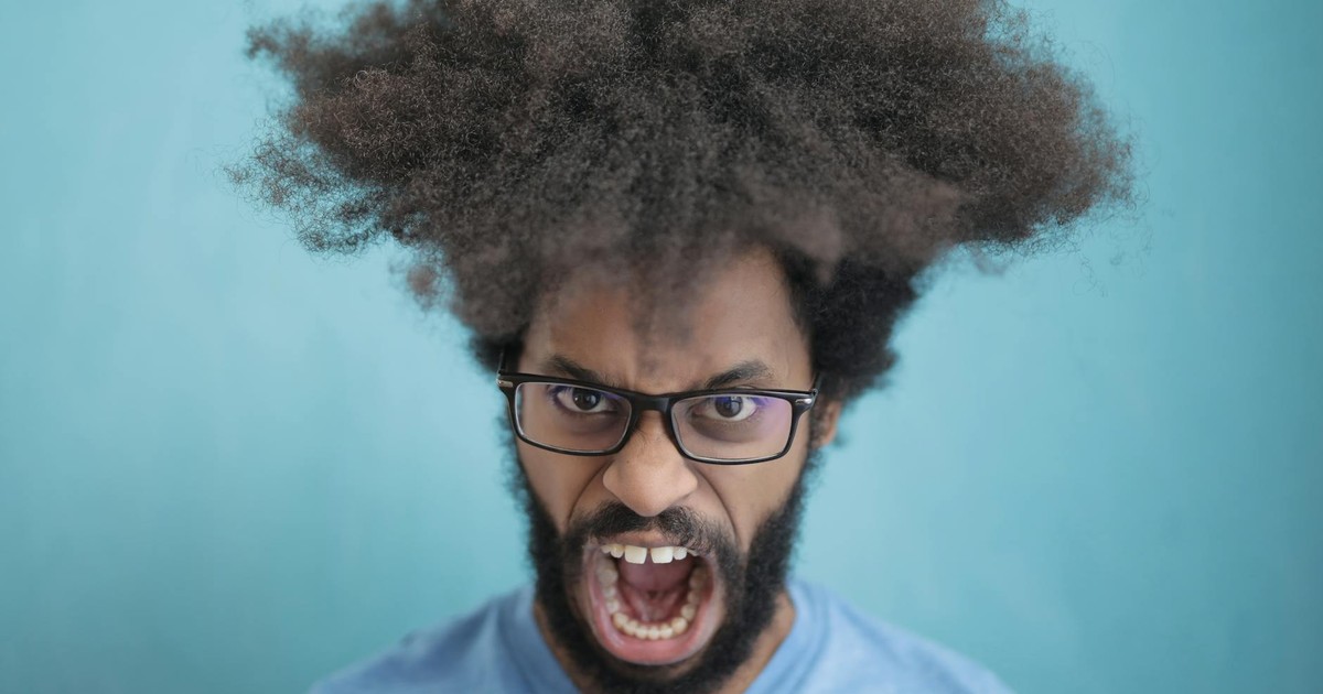 Portrait of a man with afro hair wearing eyeglasses, expressing emotion against a blue background.