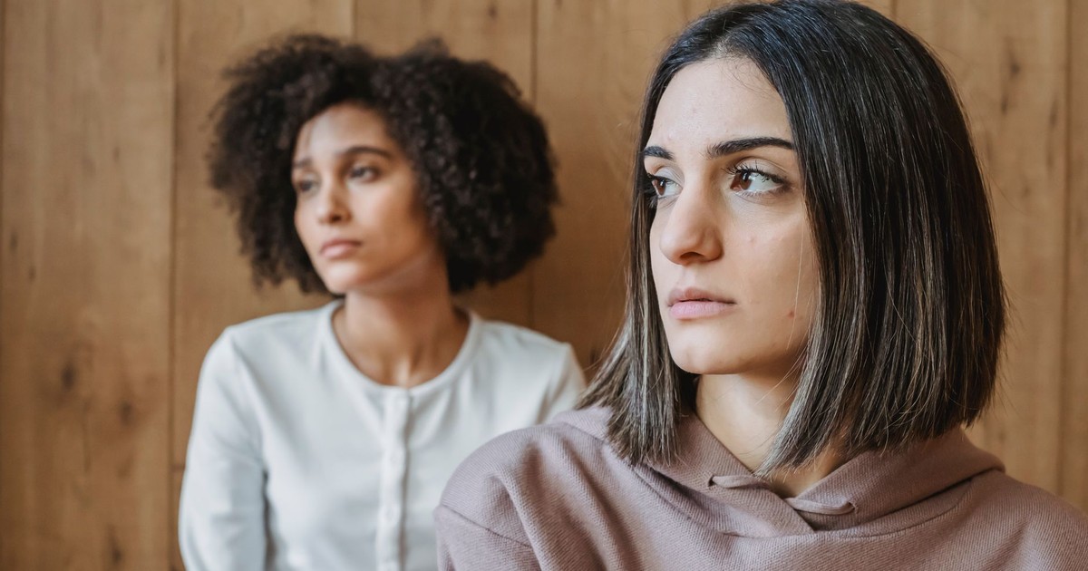 Pensive young multiracial women In casual clothes looking away against wooden wall in daylight