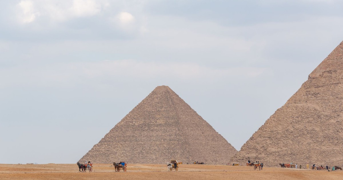 Camel riders near the iconic pyramids of Giza under a cloudy sky, showcasing Egypt's historical allure.