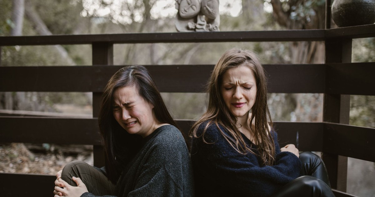 Two women experiencing emotional distress while seated outdoors during fall.