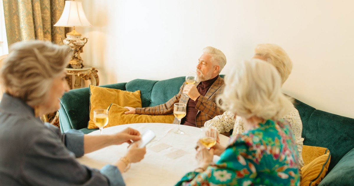 A group of senior adults enjoying wine and conversation in a cozy living room setting.