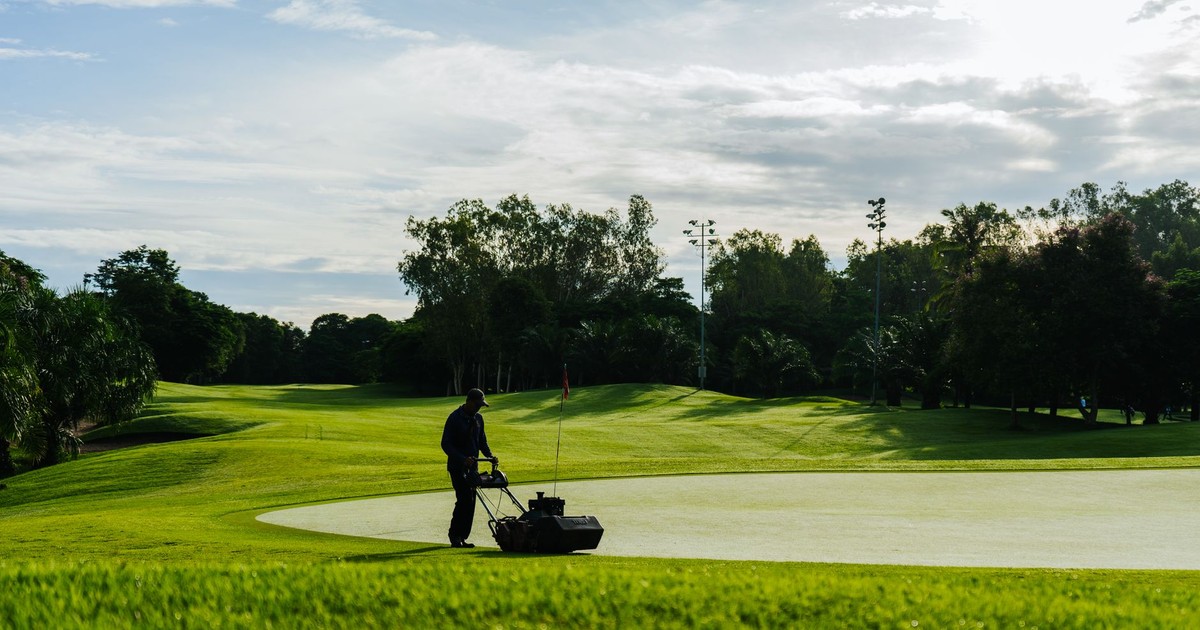 Groundskeeper mowing the green on a golf course during a sunny day, showcasing lush landscapes and maintenance.