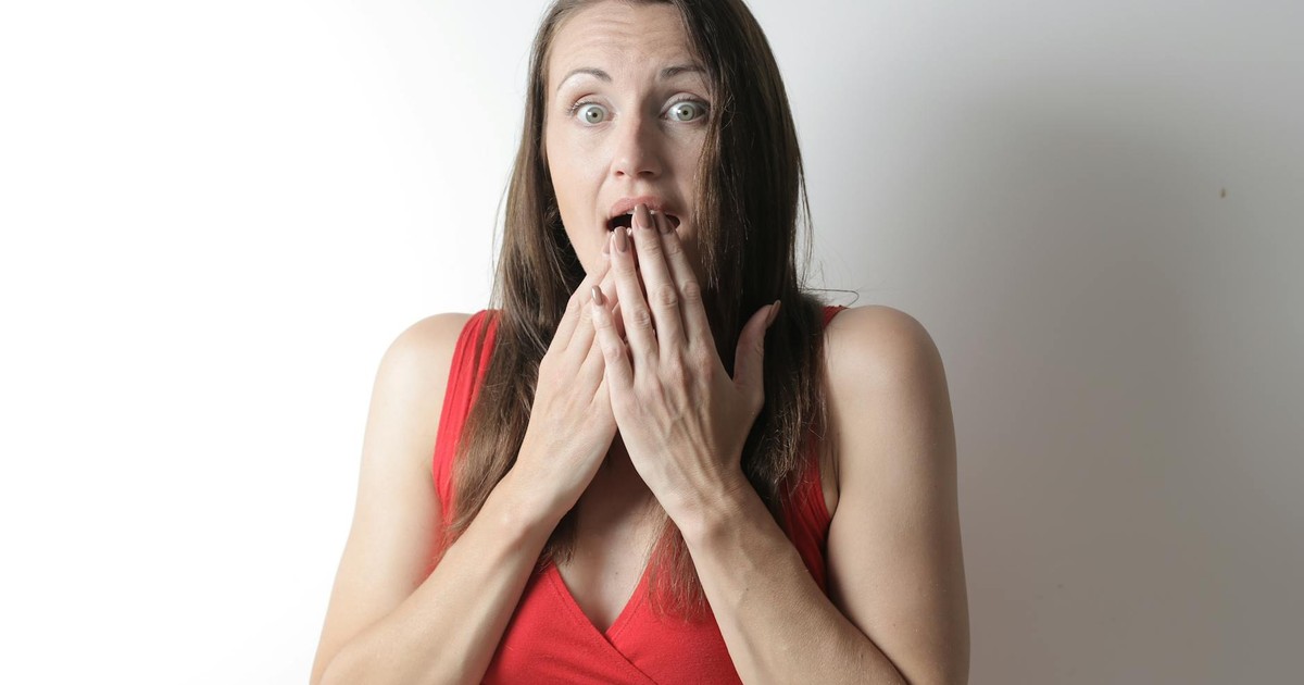 A surprised young woman in a red dress reacting dramatically against a plain white background.