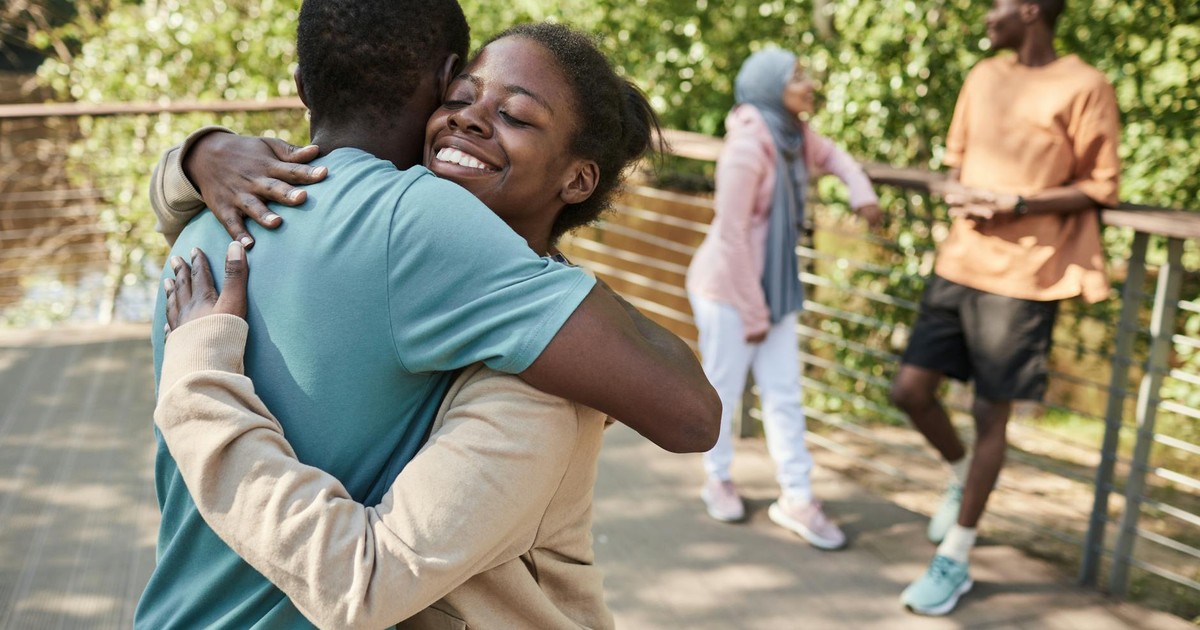 Joyful friends share a heartfelt embrace outdoors on a sunny day.