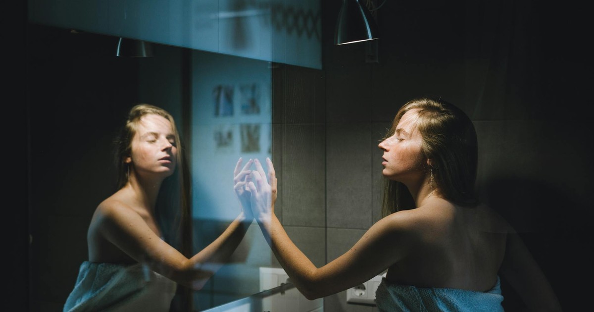 A young woman wrapped in a towel touches the mirror in a contemporary bathroom setting.